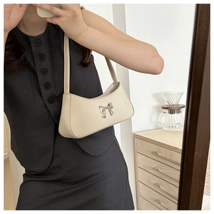 Detalle del bolso de hombro blanco crema con un lazo plateado mostrado en un selfie de espejo