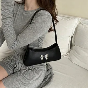 Minimalist black baguette bag with silver bow detail worn by model on shoulder