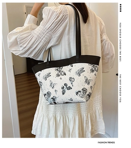 Side view of white butterfly print tote bag with black straps worn by a model in a minimalist room
