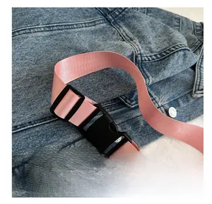 Détail d'une bandoulière rose tissée avec boucle robuste en plastique noir sur du denim