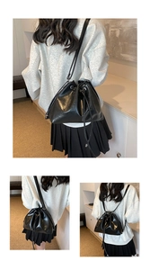 Detail of glossy black leather bucket bag showing adjustable straps and drawstring closure