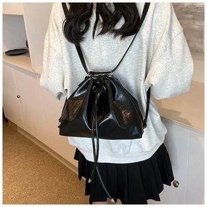 Glossy black drawstring backpack shown from a back view on a model for scale