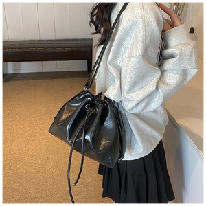 Detail view of black drawstring bucket bag in glossy PU leather with pleated texture
