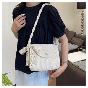 Detail of straw woven shoulder bag featuring a pearl clasp and beige lace bow accessory