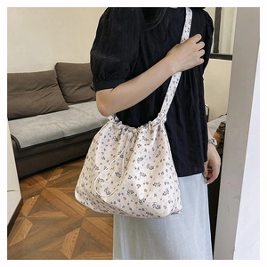 Detailed close-up of floral drawstring shoulder bag with blue patterns on cream fabric