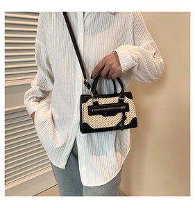 Détail du sac bandoulière en paille tressée avec bordure en cuir noir et gland sur chemise
