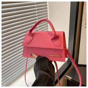Macro detail of the bright pink leather handbag with gold metal logo and sleek top handle