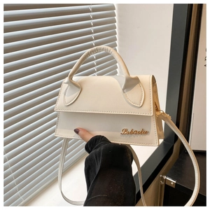 Detailed view of cream-white leather handbag with gold metal lettering and top handle