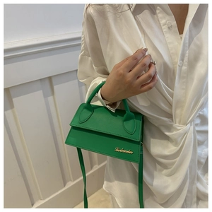 Detail of emerald green mini flap bag featuring gold logo and sleek top handle strap