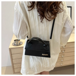 Detail of a black matte crossbody bag with golden logo worn over a white top