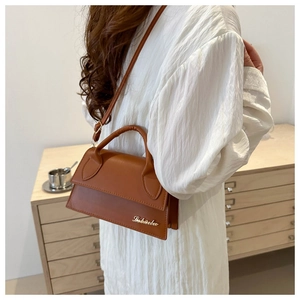 Brown leather crossbody bag detail with golden logo on envelope flap and top handle