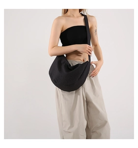 Minimalist black half-moon crossbody bag with wide shoulder strap shown on a female model