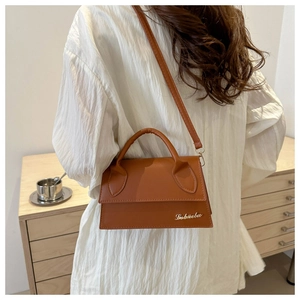 Detailed close-up of brown leather handbag with metallic logo and thin shoulder strap