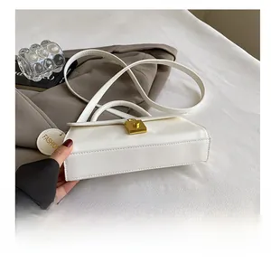 Detail view of white faux leather bag with gold rotating clasp and fashion charm