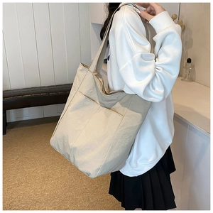 Detail of minimalist beige canvas tote bag showing the front pocket and soft texture