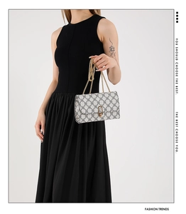 Detail of a beige chain shoulder bag with metal turn-lock on a black dress model