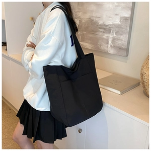 Detail of large black nylon tote bag with wide strap worn by model in minimalist setting