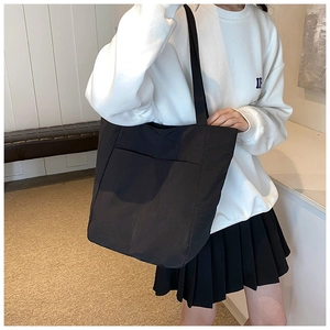 Close-up of a large black oxford tote bag with side pocket shown on a shoulder