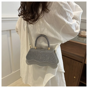 Glittering silver crossbody bag with a wavy base shown on a model in a minimalist room
