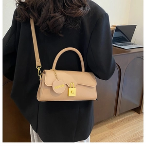 Detail of beige square handbag with gold lock and fashion tag shown on shoulder