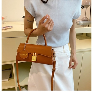 Detail of brown leather underarm bag featuring a gold clasp and 'FASHION' tag charm