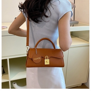Detail view of caramel brown leather shoulder bag with gold square buckle and fashion tag