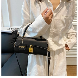 Detail of a black leather handbag with golden square lock and fashion charm on handle