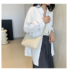 Gros plan du sac bandoulière tissé beige porté par un mannequin dans un décor d'intérieur