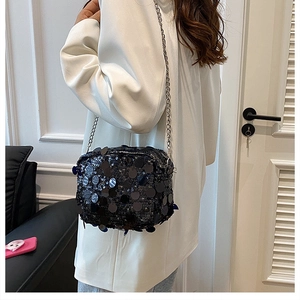 Close-up of sparkling black sequin crossbody bag with silver chain on white suit