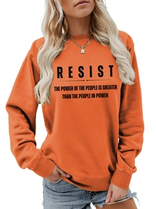 Detail eines orangenen Sweatshirts mit schwarzem Resist the Power Slogan-Aufdruck