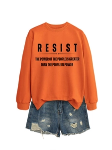 Detail von orangefarbenem Sweatshirt mit RESIST-Aufdruck und Denim-Shorts-Kombi