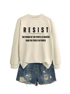 Detail eines cremeweißen Sweatshirts mit RESIST-Slogan und destroyed Denim-Shorts