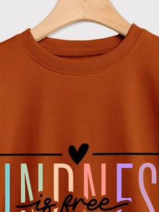 Détail de l'encolure côtelée et de l'imprimé Kindness is free sur un sweat-shirt caramel