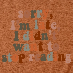 Close-up of rust red knit t-shirt featuring the slogan sorry i'm late i didn't want to stop reading