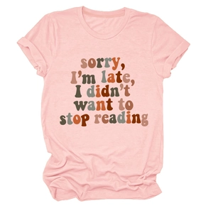 Flat lay of pink cotton T-shirt featuring vintage text 'sorry i'm late i didn't want to stop reading'
