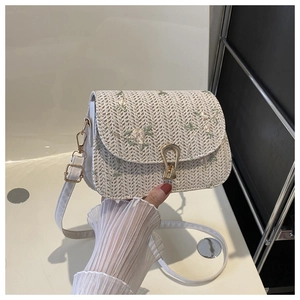 Close-up of straw woven crossbody bag featuring delicate floral embroidery and metal clasp