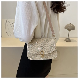Detail of straw woven crossbody bag with pink flower embroidery and gold buckle hardware