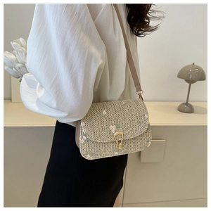 Detail of floral embroidery and gold metal buckle on beige woven straw shoulder bag