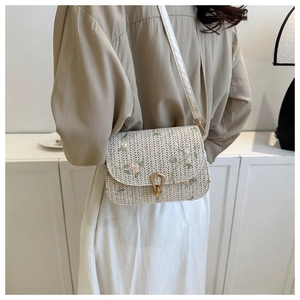 Detailed view of straw texture with floral embroidery and gold metal clasp on crossbody bag