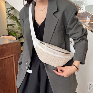 Sac banane tissé beige avec bandoulière blanche porté sur un blazer gris pour l'été