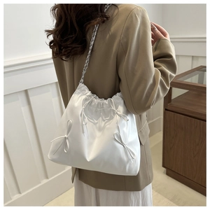Close-up of white pleated bucket bag with bow details and silver chain strap texture