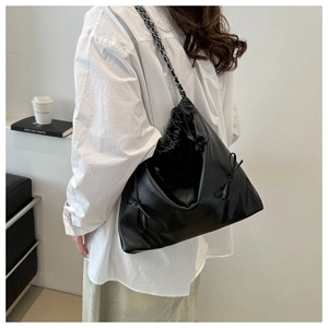 Detailed side view of black pleated handbag with bow detail and metal chain strap on model