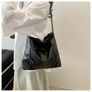 Detail of black pleated drawstring bucket bag with decorative side bows and chain strap