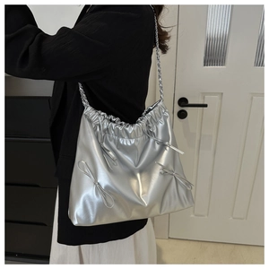 Detail of silver metallic leather handbag featuring decorative bows and chain strap