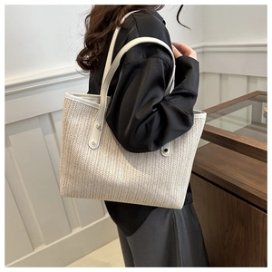 Detail of hand-woven straw tote bag with white leather straps and silver metal rivets
