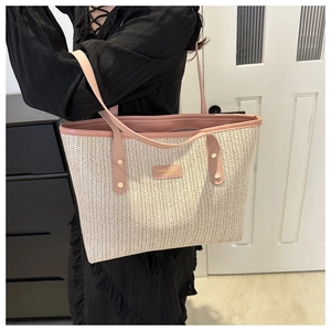 Detailed view of straw tote bag with pink leather handles and metallic rivet accents