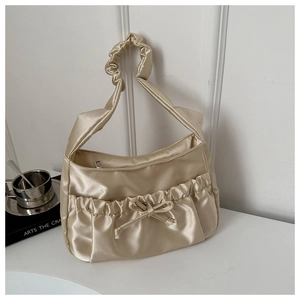 Detail of champagne gold pleated satin underarm bag with bow decoration and smooth texture