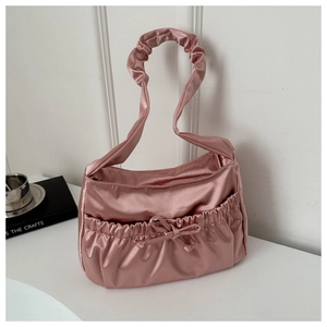 Close-up of pink satin shoulder bag featuring elegant pleats and decorative bow details