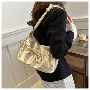Detail of champagne satin pleated shoulder bag featuring a decorative bow and soft texture