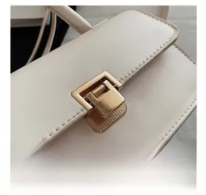 Makro-Detail der goldenen Metallschließe und feinen Nähte an der cremefarbenen Ledertasche